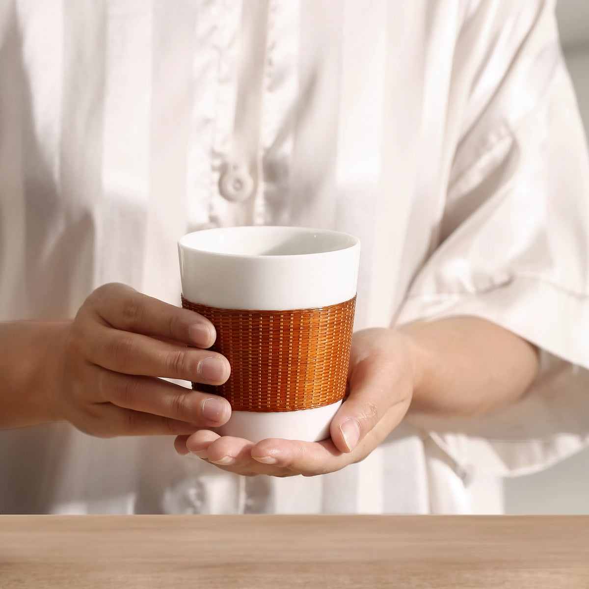A hand holding the THE YUNXI Daily Cup in Baked, showing its size and woven bamboo sleeve.