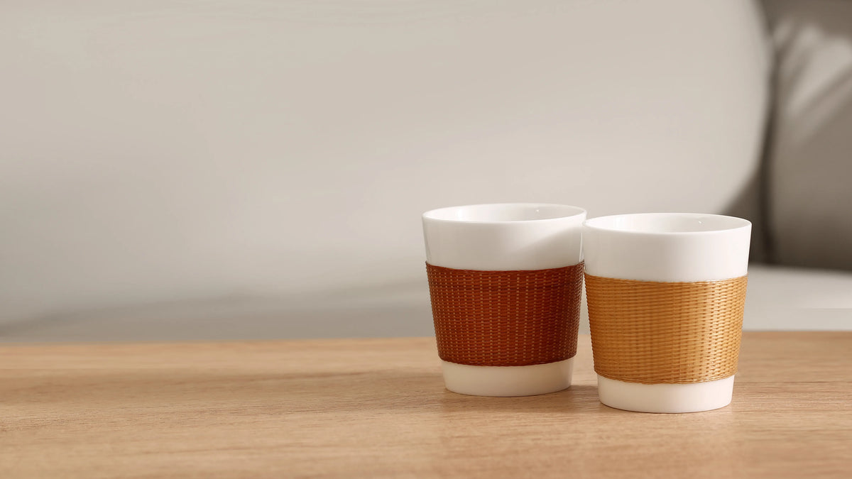 THE YUNXI Daily Cup in Baked and Natural, featuring woven bamboo sleeves over white porcelain.