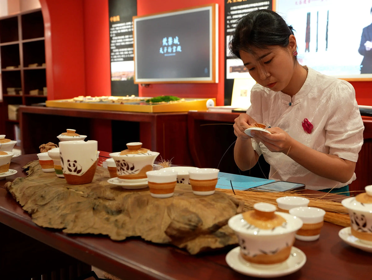 Liu Luolin weaving bamboo beside a bamboo-wrapped porcelain tea set with panda motifs.