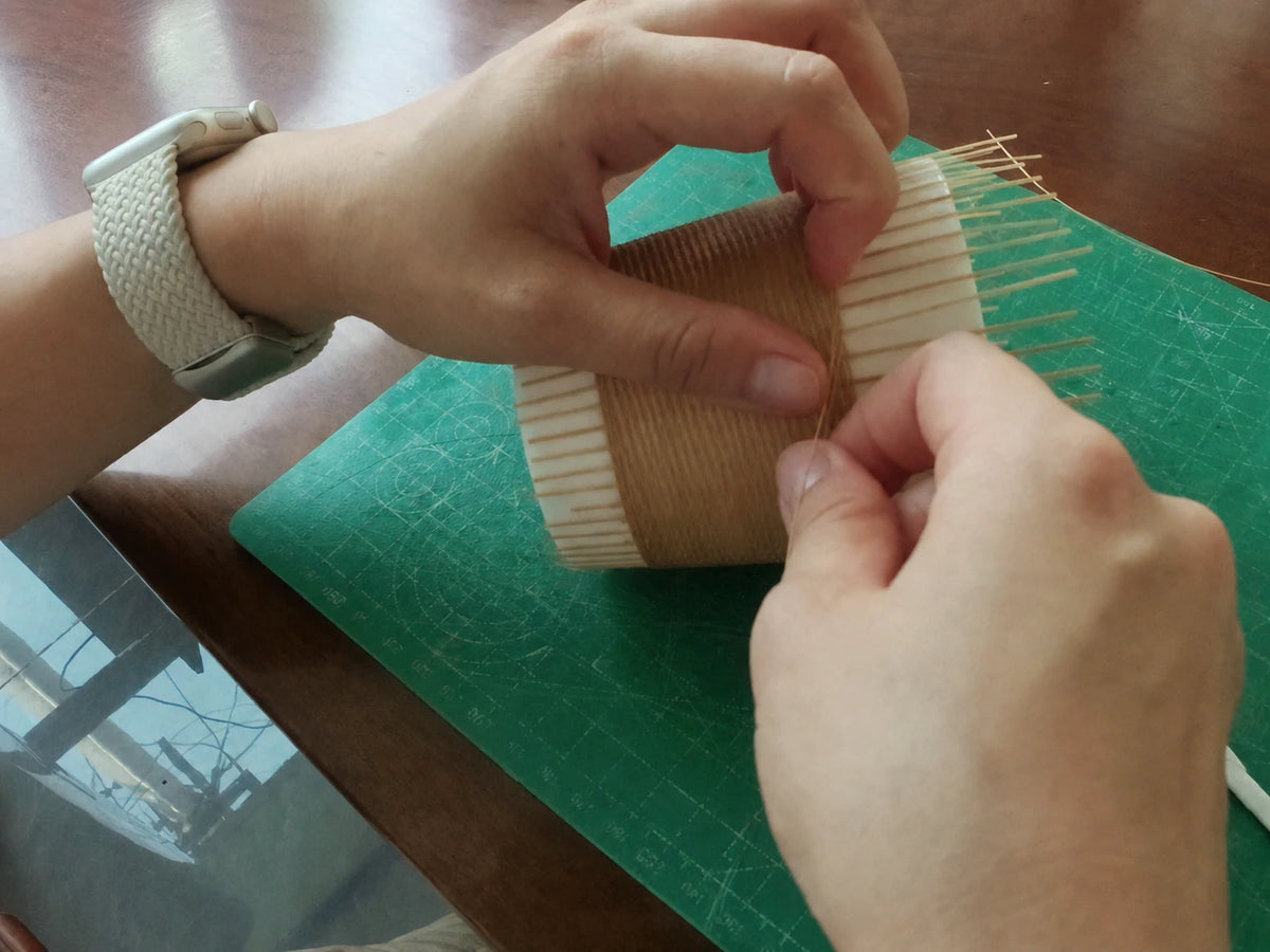 Hands weaving fine bamboo filaments around a porcelain Daily Cup