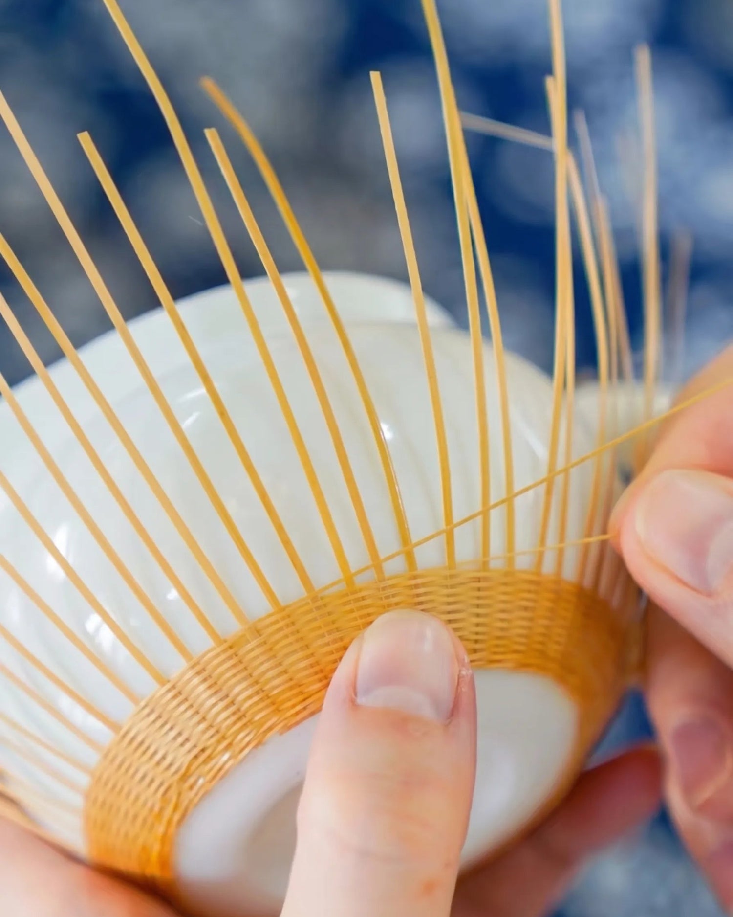Artisan handweaving bamboo strips around a white porcelain cup for THE YUNXI Bamboo over Porcelain collection.