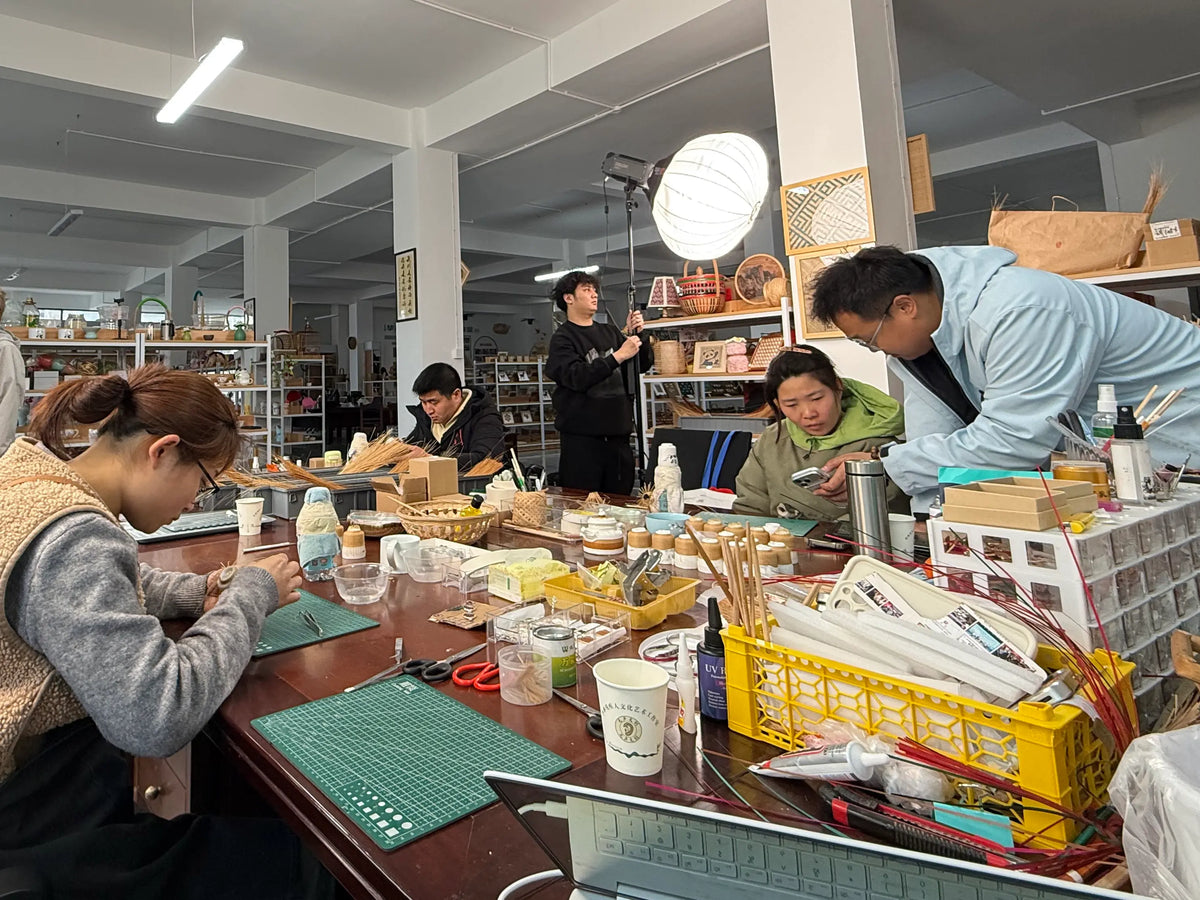 People working on bamboo-wrapped porcelain vessels at a shared workbench with tools and materials.